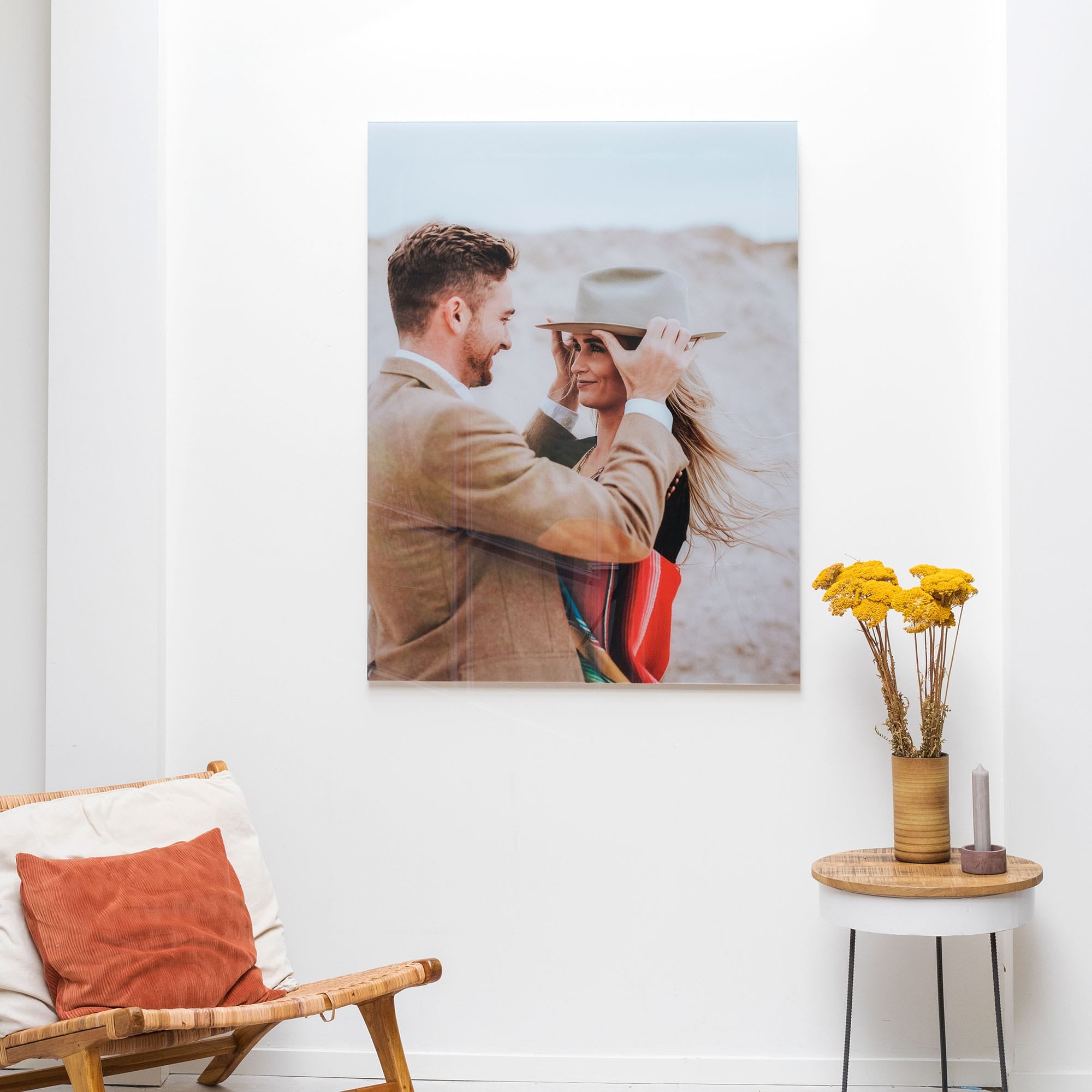 Fotovergroting Plexiglas Portrait 3:4 van knuffelend koppel op witte muur, met gele droogbloemen op tafel