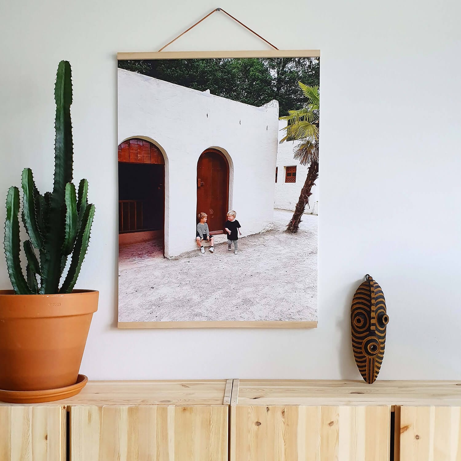 Fotovergroting Poster Portrait 3:4 met houten rand in modern interieur; afbeelding van een witte gevel met bogen en twee kinderen bij de deur.